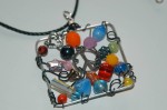 Fun glass beads, metal charms, and black wire form this crazy collage. Hangs from 21" black cotton cord. Pendant measures 2" square.
