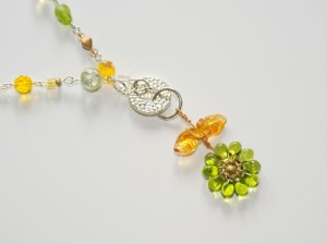Dainty flower hangs from 17" beaded chain in shades of yellows and greens. Pendant hangs 2".