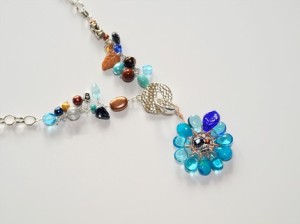 Flower pendant in shades of blue has a tiny bead and wire collage in the center, and hangs from 17" chain full of bead charms.