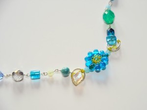 32" strand of delicious aquas accented with yellow and silver. A mini wire wrapped flower nestles along the way.